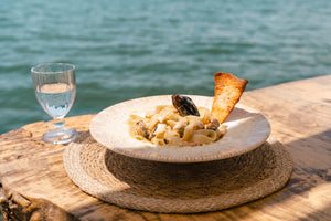 Pasta dish with a glass of water on a wooden table by the water